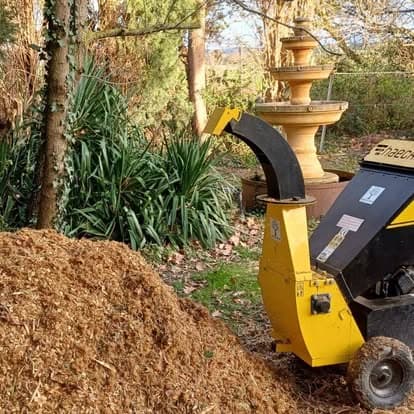 Broyeur de branches en fonctionnement dans un parc, à côté du tas de broyat produit sur place